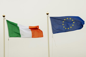 Waving flag of Euro Union and Republic of Ireland on grey sky background.