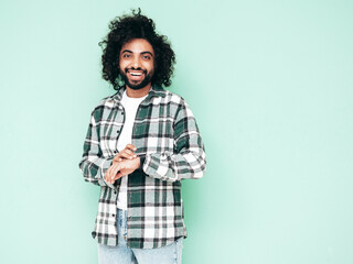 Handsome smiling hipster  model.Sexy unshaven Arabian man dressed in summer stylish shirt and jeans clothes. Fashion male with long curly hairstyle posing near green wall in studio. Isolated