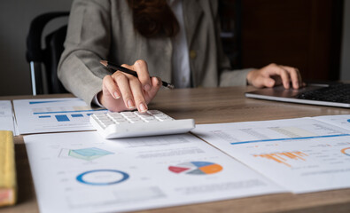 Close up of Businesswoman or auditor using calculator calculate business reports and paperwork chart on desk in workplace, Accountant making financial statements, financing and accounting concept.