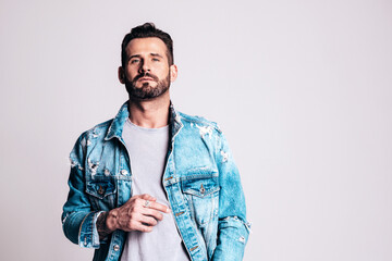 Portrait of handsome confident stylish hipster lambersexual model. Sexy man dressed in jeans jacket. Fashion male isolated on grey in studio