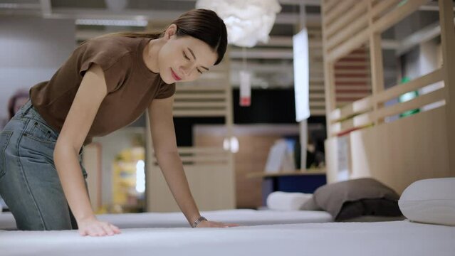 Young beautiful woman choosing mattress at retail furniture store new home. Housewife touching softness test buying bedding for family. Female checking quality shopping bed in mattress store hall.