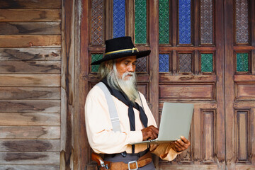 Portrait of old man in cowboy hat  with notebook standing against in vintage cowboys village...