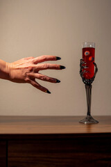 Witch hand with long black nails take glass of wine with eyeballs from the table. Halloween...