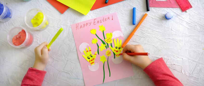 Child creating card with Easter funny eggs and flowers from colorful paper. Handmade. Project of children's creativity, handicrafts, crafts for kids. Happy easter text