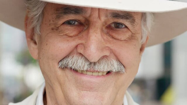 Cowboy, texas and western with a senior man outdoor wearing a hat and a smile on his face. Portrait, rodeo and USA with an elderly male farmer standing outside on a farm or ranch on a blur background