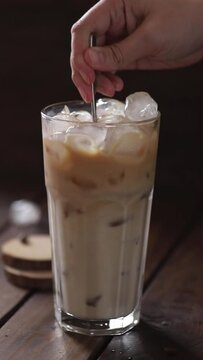 Ice Latte. Step 4. Stir The Coffee, Ice And Milk With A Spoon. A Hand Stirs A Spoon Of Iced Coffee And Milk In A Tall Glass.