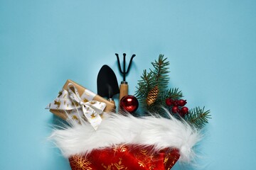 Christmas and new year composition. Garden tools, shovel and rake with gift box, fir tree branch in...