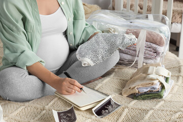 Pregnant woman preparing list of necessary items to bring into maternity hospital on bed at home,...