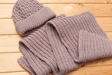 Fototapeta na wymiar knitted scarf and woolen hat women's winter set in beige tones on a wooden background.