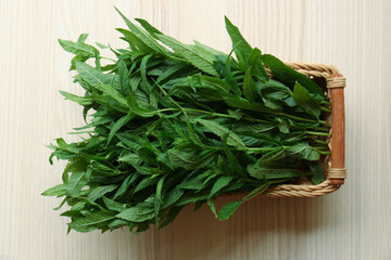 Beautiful green mint in wicker basket on white wooden table, top view