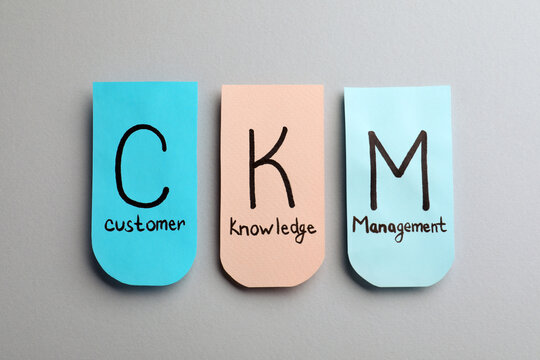 Notes with abbreviation CKM (Customer Knowledge Management) on light background, flat lay