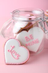 Glass jar and decorated heart shaped cookies on pink background. Valentine's day treat