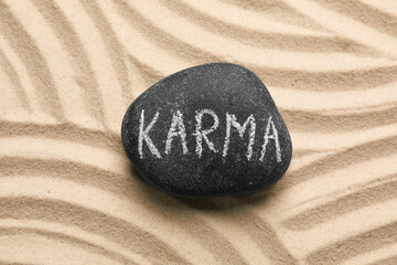 Stone with word Karma on sand, top view