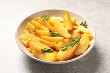 Plate with tasty baked potato wedges and rosemary on grey table, closeup