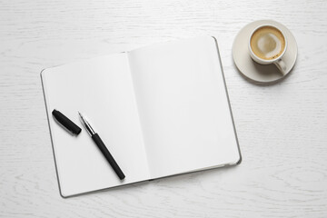 Open blank notebook, pen and coffee on white wooden table, flat lay