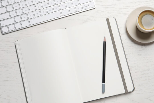 Open blank notebook, pencil, coffee and keyboard on white wooden table, flat lay
