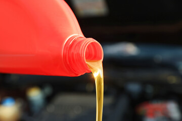Pouring motor oil from red container on blurred background, closeup. Space for text