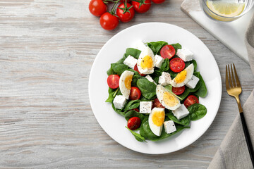 Delicious salad with boiled eggs, feta cheese and tomatoes served on wooden table, flat lay. Space for text
