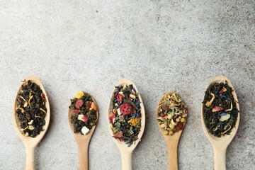 Different kinds of dry herbal tea in wooden spoons on light grey table, flat lay. Space for text