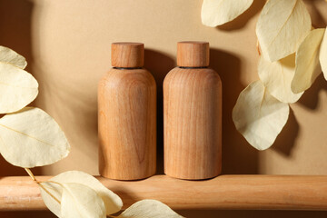 Fototapeta na wymiar Wooden bottles of cosmetic product and dried leaves on dark beige background