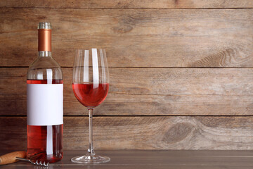 Corkscrew near bottle and glass of delicious rose wine on table against wooden background. Space...
