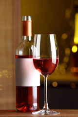 Bottle and glass of delicious rose wine on wooden table in bar