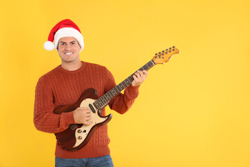 Man in Santa hat playing electric guitar on yellow background, space for text. Christmas music