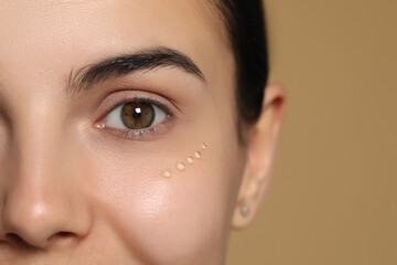 Young woman with gel on skin under eye against beige background, closeup