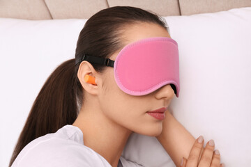Young woman with foam ear plugs and mask sleeping in bed, closeup