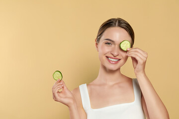 Young woman with cucumber slices on beige background, space for text. Eye skin care