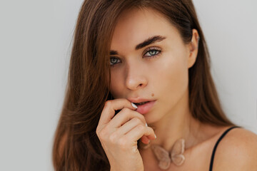 Fototapeta premium Close up portrait of seductive bunette woman posing over white wall. Healthy long hairs. Fashionable necklase.