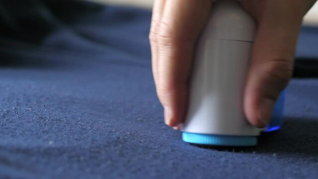 Womans hand, holding a machine for removing pellet and pools from clothes and fabric, uses on a dark blue knitted men's pants. A modern electronic device for updating old things. Textile care concept.