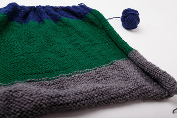 Knitted clothing, accessory in process of making. Knitting needles and ball of threads, yarn on white background. Striped blue, green, grey cloth