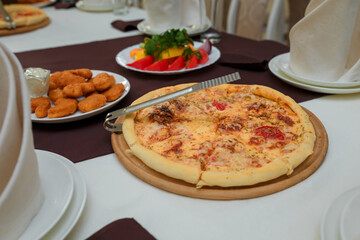 Festive table with appetizers for children. Chicken nuggets with sauce, plate with vegetables and greenery, pizza.