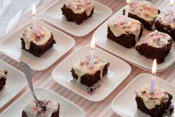 Kerzen leuchten auf kleinen Stücken Schokoladenkuchen mit weißer Schokolade und rosa Dekoration