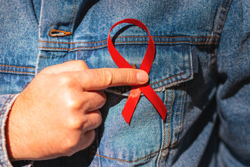 Man wearing Denim Jacket holding a red AIDS awareness ribbon on his chest. World Aids Day and World Diabetes Day Concept of healthcare and medicine.