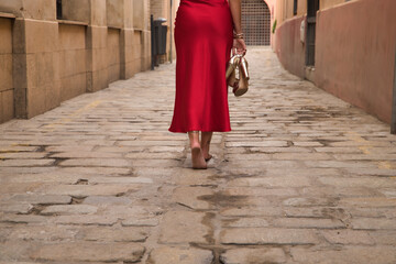 Detail of woman with her back turned, wearing an elegant red party dress and holding golden high...