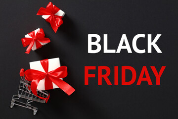 Fototapeta na wymiar Black friday sale concept. Shopping cart with gift boxes and sign Black Friday on black background.