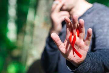 Smoking Man holding red aids ribbon in hand at summer day.World aids day concept.