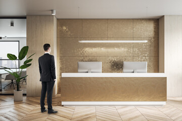 Businessman back view on golden shade wall in reception area with modern computers, wooden parquet floor and green plant