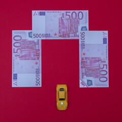 500 euro banknotes lined up above a yellow car on a red background with copy space. Minimalistic crisis scenes.