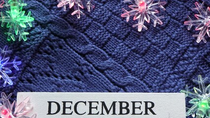 December text on white wood block on blue knitted sweater with star shaped Christmas lights. Christmas and hello December Concept.