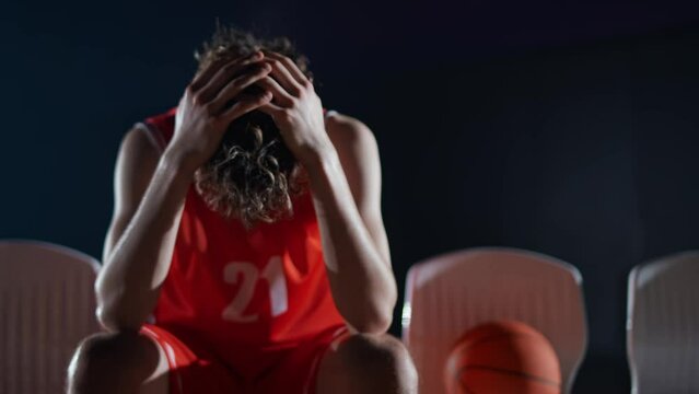 Slow motion, an tired basketball player recovering from an basketball match, sad man sitting on a bench.
