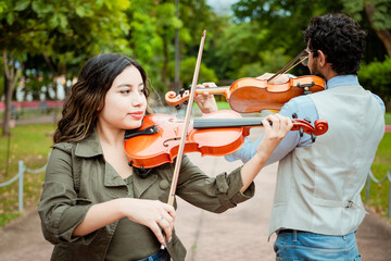Two young violinists standing playing violin in a park. Portrait of man and woman together playing...