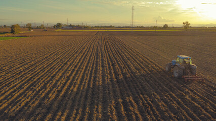 aerial view of farmer driving tractor deep plowing land at sunset, Piacenza, Italy 