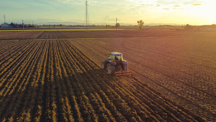 aerial view of farmer driving tractor deep plowing land at sunset, Piacenza, Italy 