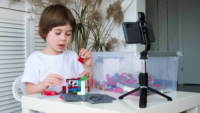 Little 5 year boy is filming his game of building constructor blocks on his smartphone. The child is broadcasting video to social networks. Kid blogger communicates with his online audience. Blogging.