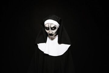 Fototapeta na wymiar Portrait of scary devilish nun on black background. Halloween party look