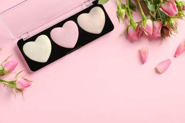 Palette of heart shaped eyeshadows and roses on light pink background, flat lay. Space for text