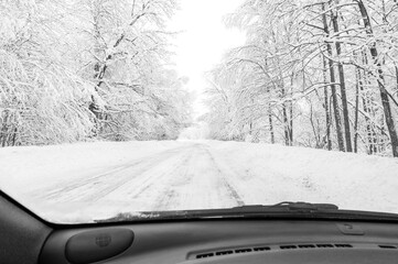 Road trip concept. View through car window on road in snowy forest. Driving on a snowy country road in daytime.